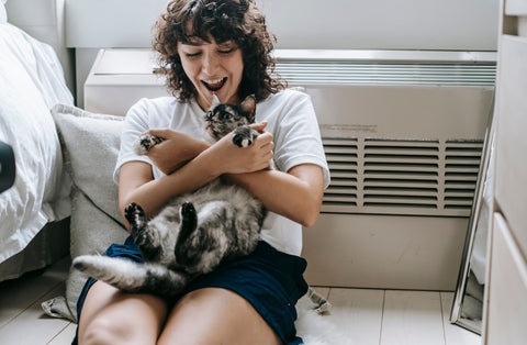 Vrouw speelt en knuffelt met haar kat in de woonkamer